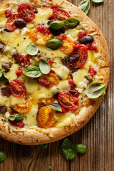 Close up view of the vegetarian pizza with cherry tomatoes, kalamata olives and fresh basil on a wooden background.