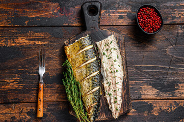 Roasted fillets of mackerel fish on cutting board. Dark wooden background. Top view