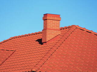 Naklejka premium Red roof tiles with red brick chimney on blue sky background.