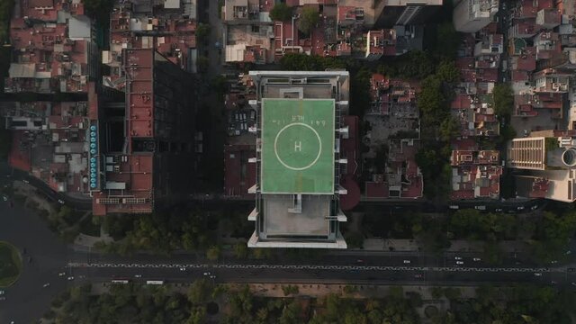 Aerial birds eye overhead top down view of tall office building with green heliport on top and surrounding area. Camera zooming out. Mexico city, Mexico.