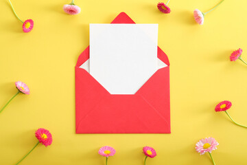 Red open envelope with blank paper card mockup and wildflowers on yellow background. Flat lay composition, top view, copy space. Love letter, romance cocnept.