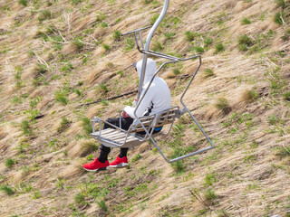 A man in red sneakers and a white jacket descends the chairlift without lowering the safety rail....