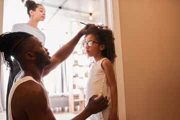 Man with dreadlocks measuring height of his curly little daughter