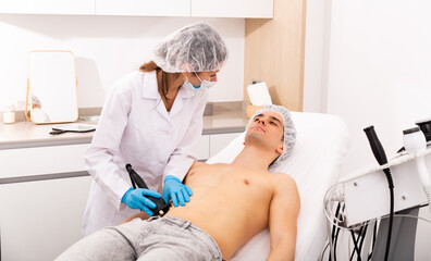 Obraz na płótnie Canvas Young man receiving ultrasound fat cavitation procedure on his abdomen in aesthetic cosmetology clinic