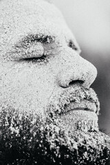 creative portrait of a man with a beard whose face is covered with a layer of sea sand