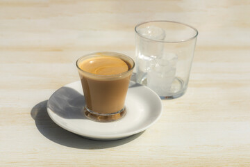 detail of a glass of coffee cut with milk together with a glass with ice cubes to make a refreshing summer drink on a light wood table