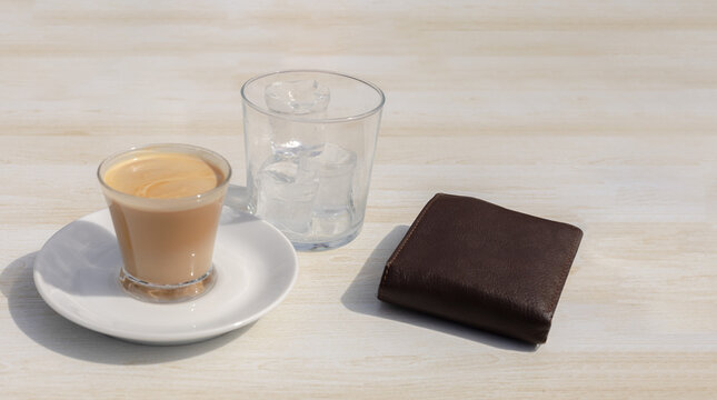 cup of coffee with milk and a glass of ice on a table in a cafeteria together with a wallet with money to pay for the drink