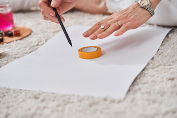 Woman sitting at the floor and outlines with a pencil some shapes for her drawing