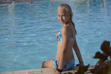 Teenage blonde girl sit in pool and smile