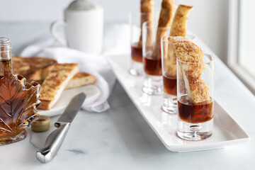 A row of french toast shot glass appetizers against a bright sunny window with ingredients on the side.
