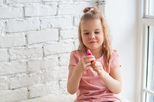 Portrait of preschool-aged caucasian girl puts on the lips hygienic lipstick