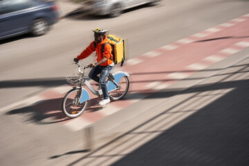 Naklejka premium Male person with yellow backpack riding bicycle to his client
