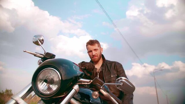Young man sitting on motorcycle on the road at sunset, slow motion