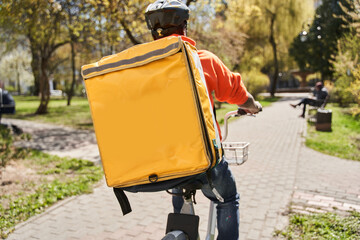 Courier with yellow backpack riding at the bicycle and looking for a way to the client
