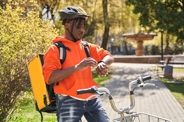 Courier wearing helmet standing with thermo bag at his bicycle