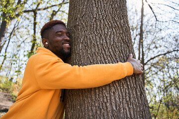 Man relaxing in the forest and hugging a tree at the great sunny day