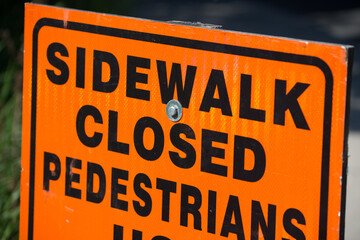orange and black construction sign with: sidewalk closed and pedestrians...
