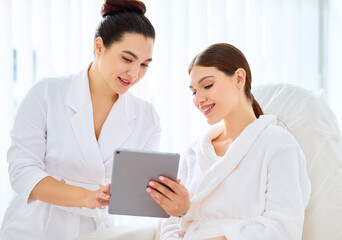 Cosmetologist and woman using tablet in clinic