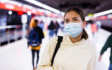 Fototapeta na wymiar Portrait of an active girl in a protective mask, walking on a subway platform during a pandemic, with a backpack..on her bask. Close-up portrait