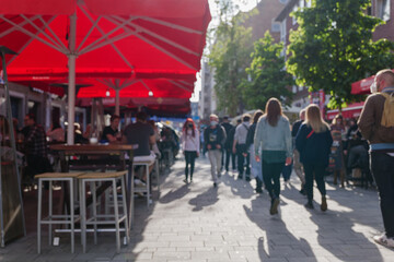 Selected focus view at Red and white caution tape restrict outdoor seating area in old town Düsseldorf, Germany during lockdown. Crowd of people enjoy reopening restaurant during epidemic COVID-19. 