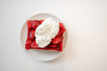 Top view at traditional German sliced fresh strawberry cake tart or pie on topped with whipped cream, on white table.