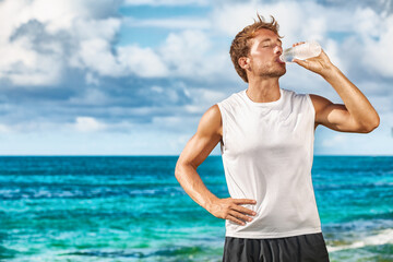 Sports drink fitness man drinking water botlle during outdoor exercise workout on beach. Dehydrated...