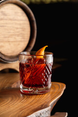 American old fashioned cocktail garnished with an orange zest, wooden barrel on a background, unusual creative wooden table