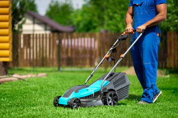 Lawn grass mowing. Worker cutting grass in a green yard. A man with an electric lawn mower mowing a...