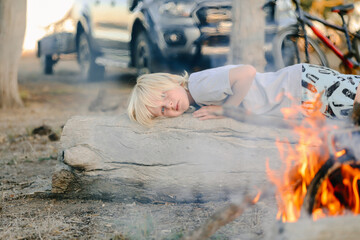 Obraz na płótnie Canvas Little boy lying on log in front of campfire in the Australian bush