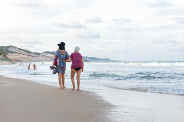 Mulher idosa caminhando na praia com companhia familiar