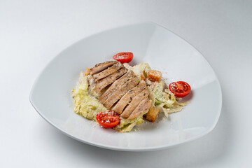 Classic caesar salad with crunchy lettuce and a whole grilled chicken breast, isolated on white background in a studio