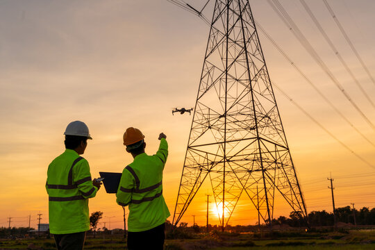 Team work of Engineers location help Technician use drone to flying inspect equipment instead of workers at the high voltage electric transmission tower, electric power station