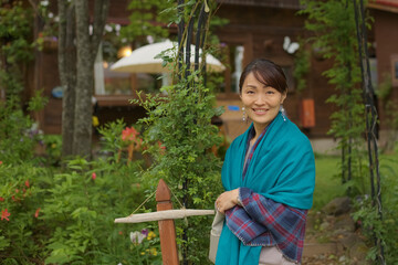 A Japanese woman in front of an outdoor yard wearing a blue shawl.
