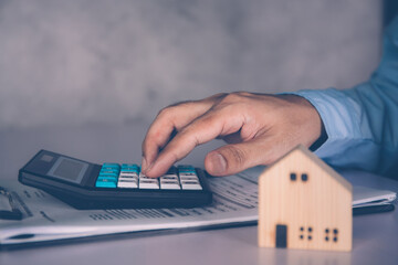 Businessman calculate with calculator about investment and having document on clipboard and home model on desk, insurance and finance, planning about real estate and residential, business concept.