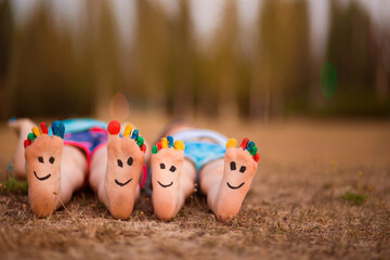 Two little child have fun lying outdoor on grass. Feet of child with painted smile faces.