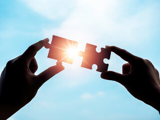 Jigsaw puzzle against blue sky background, silhouette. Two hands of businessman connecting two...