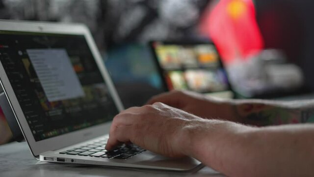 A person typing on a silver MacBook Air laptop computer on YouTube, at a white desk with iPad screen in back ground, working from home after Covid 19 pandemic lockdown restrictions. In 4k 60fps.