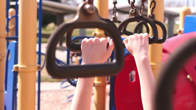 Kid hands little Caucasian girl or boy playing on children&rsquo;s playground curved yellow monkey bars at park on sunny spring or summer day after school let out, or at recess. In 4k slow motion.