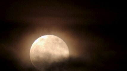 Nighttime closeup of full moon rising, while being enveloped by ominous clouds