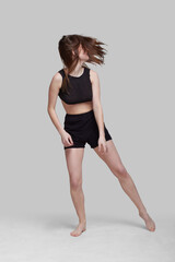 Young slim athletic girl, with long hair, in a black top and shorts, dancing in the white studio. motion blur