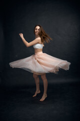 Fototapeta na wymiar Young girl in white top and peach skirt dancing in black studio