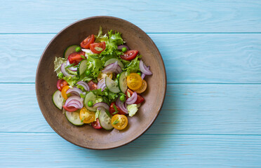 Mixed salad leaves, red and yellow tomatoes, cucumber and red onions salad in rustic plate