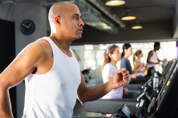 Fototapeta na wymiar Portrait of sporty young adult man running on treadmill in gym