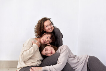 Content mature mother hugging adult daughters on white background in studio and looking at camera