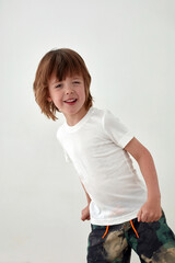 Happy boy in casual white t shirt standing against white wall and looking at camera