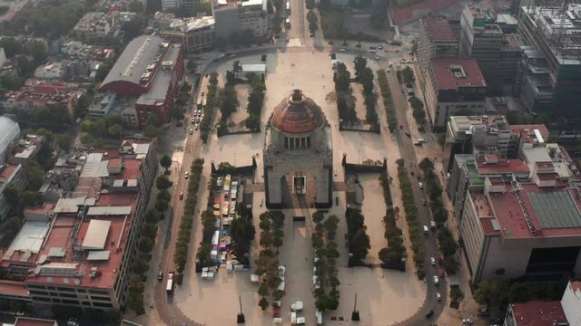 Aerial view from drone on famous Monument to Revolution on Plaza de la Republica. Camera angle tilting up to city panorama against sun. Mexico city, Mexico.