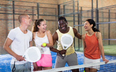 Happy four male and female partners of padel tennis posing at tennis court