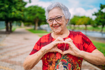 Joyful senior lady in glasses laughing heart with hands. Latin American woman. Brazilian elderly woman. - obrazy, fototapety, plakaty