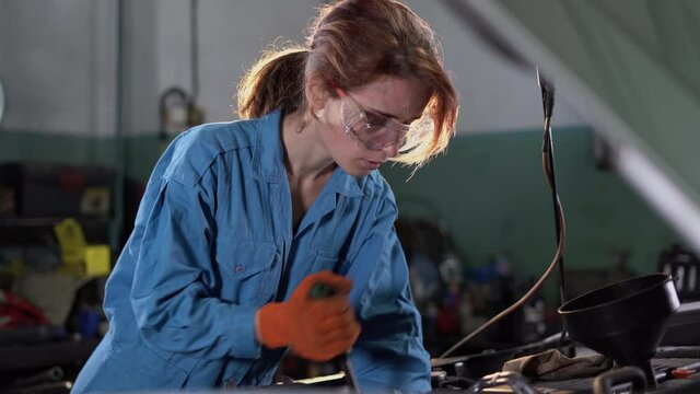 Portrait of a woman mechanic working in a car service. Empowering a woman repairing an engine. Open trunk, engine repair. spin the ratchet. A real atmospheric workshop.