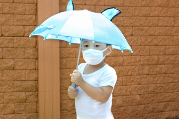 Little Asian boy holding an umbrella and wearing face mask protection from influenza and...